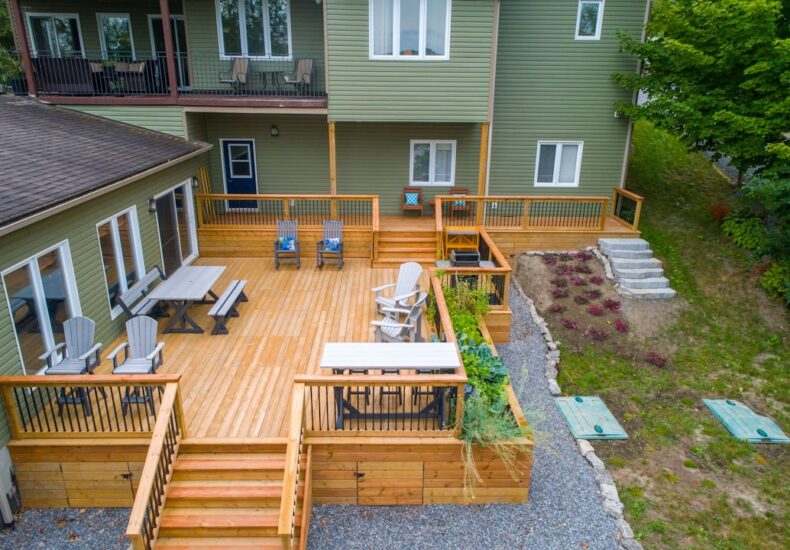 a deck with chairs and tables on it next to a house
