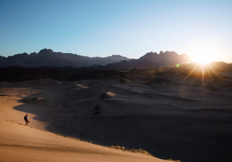 a person is walking in the desert at sunset