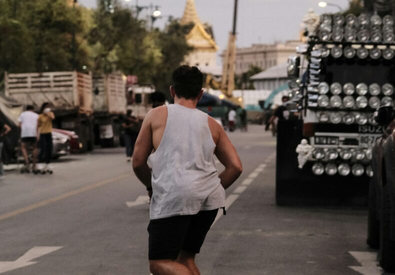 man in white tank top and black shorts running on road during daytime