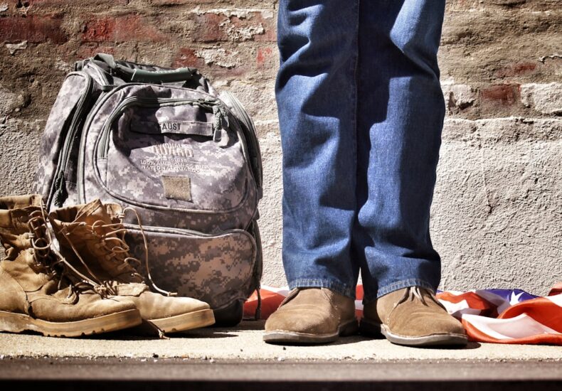 minimalist photography of person standing near backpack and boots