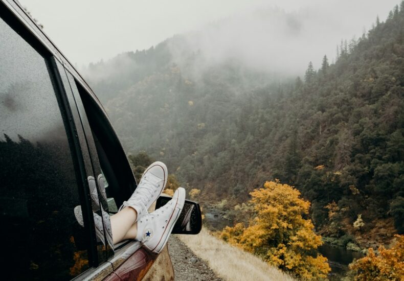 person's feet wearing white Converse sneakers on car door