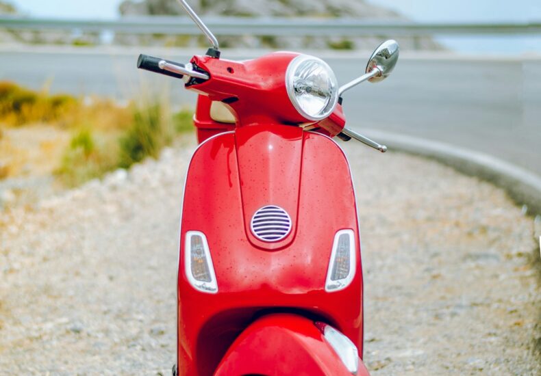 red Vespa motor scooter on side of the road