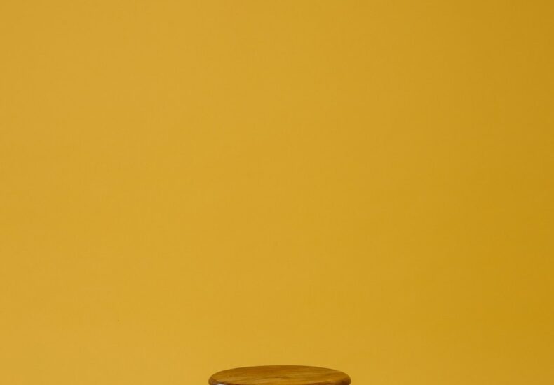 round brown wooden top and black base chair on yellow background