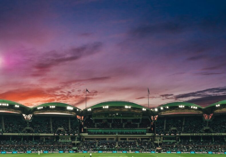 people watching game of cricket during sunset