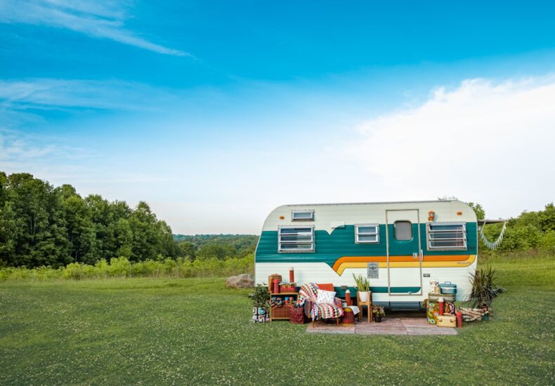 white and blue rv trailer on green grass field under blue sky during daytime