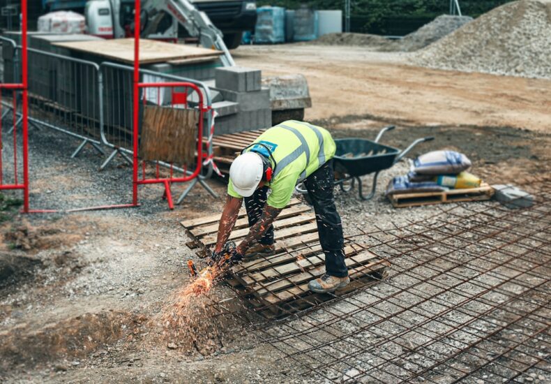 man in green and yellow safety vest and blue denim jeans standing on brown wooden pallet