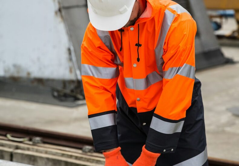 a man in an orange safety jacket working on a metal rail