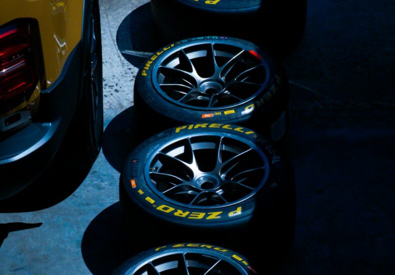 Four racing tires stacked next to a yellow vehicle