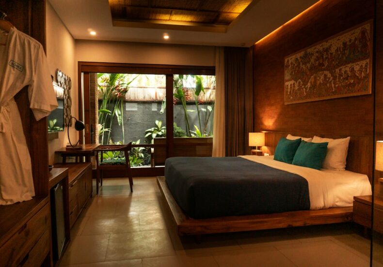 A hotel bedroom with a wooden bed, teal pillows, and a private garden view