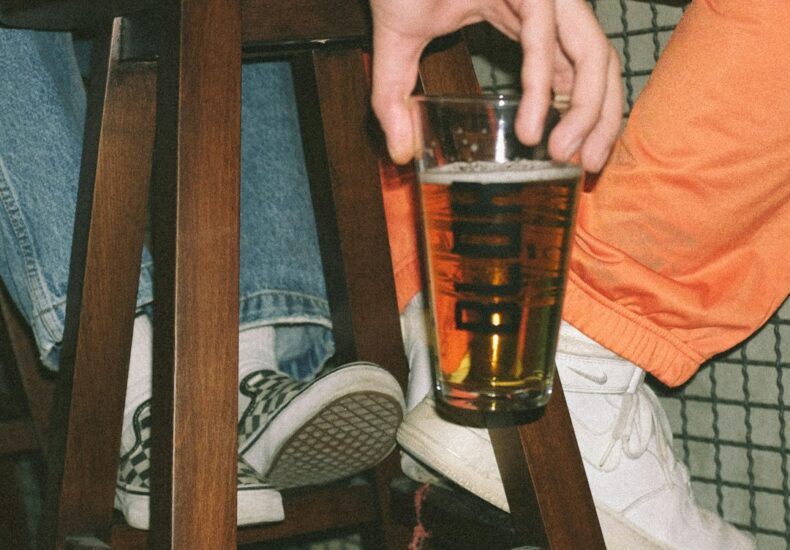 person holding clear drinking glass with brown liquid
